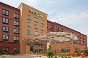 A Holiday Inn hotel with a brick facade, a covered entrance, and a landscaped area with flowers. - Holiday Inn Madison at The American Center by IHG (Madison)