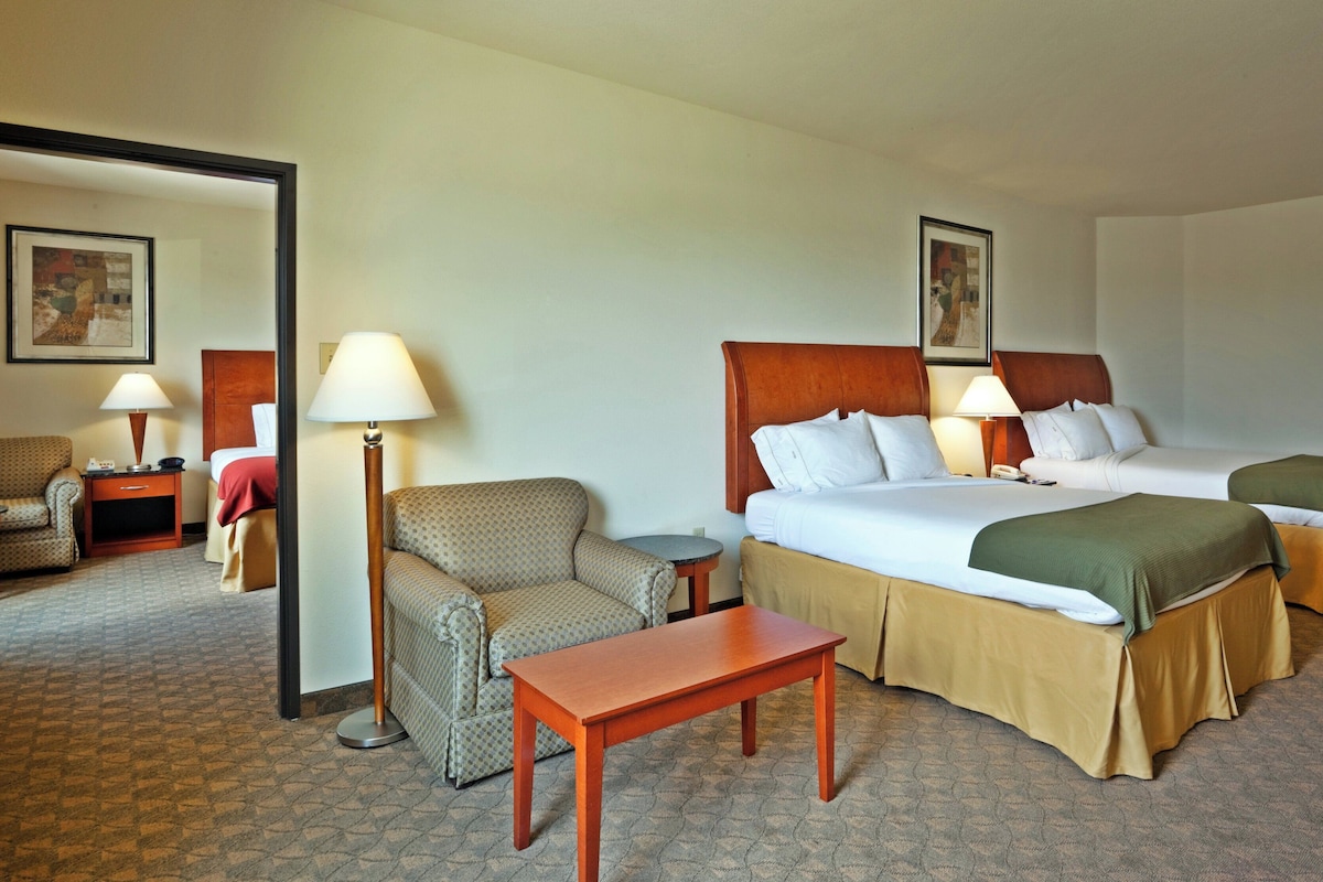 A hotel room with a bed, two bedside tables, a chair, a small table, and a lamp.