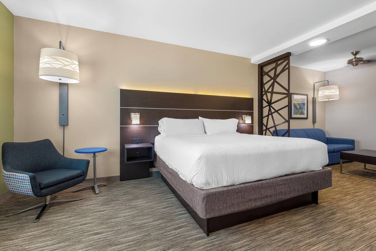 A modern hotel room with a large bed, a desk, a chair, and a sofa.