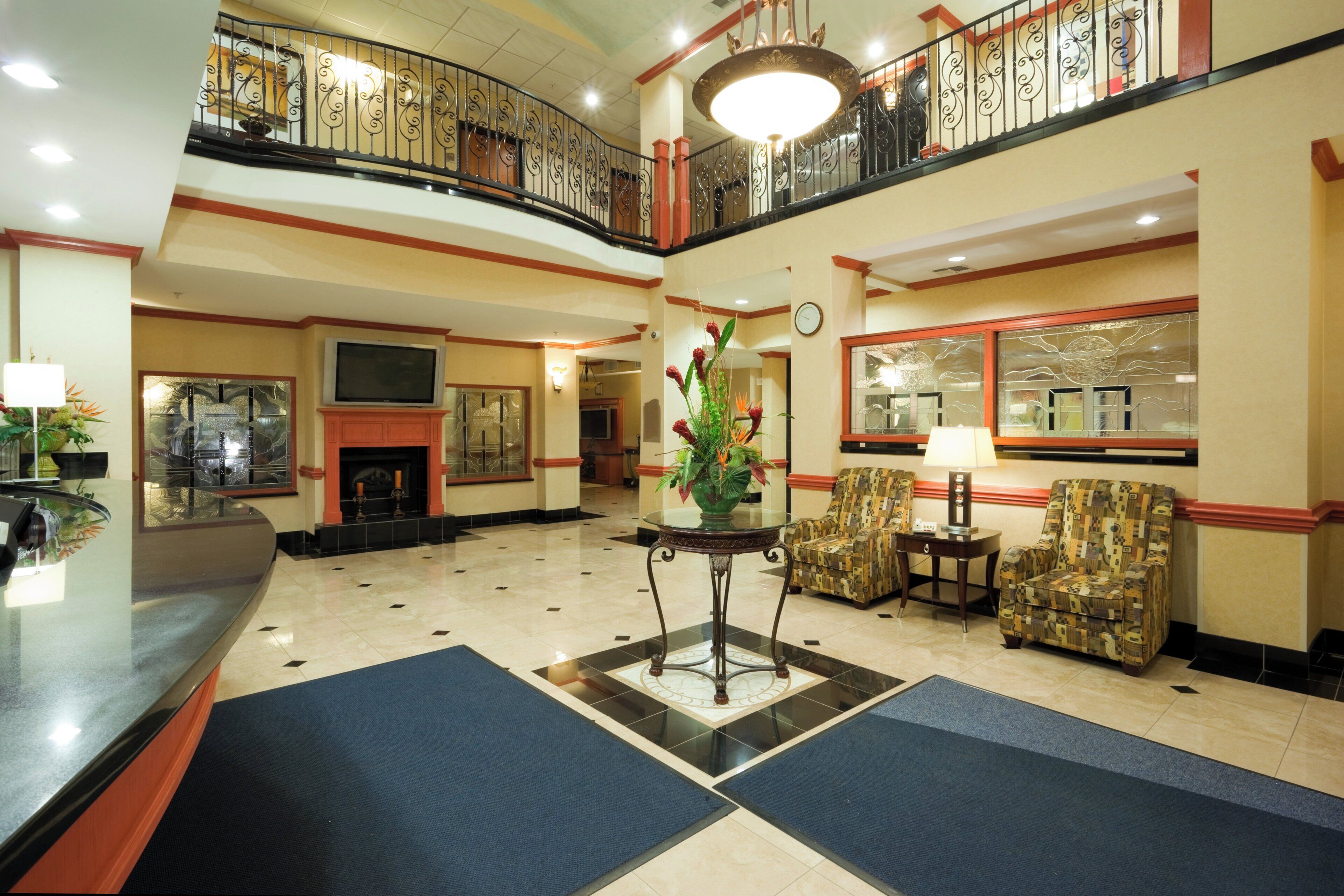 Un vestíbulo de hotel con mostrador de recepción, zona de estar, plantas decorativas y chimenea.