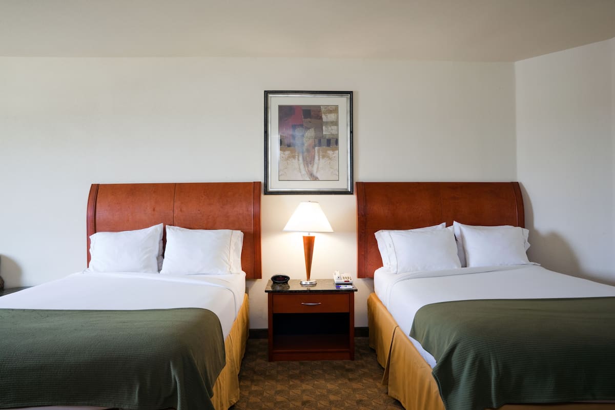 A hotel room with two beds, a nightstand with a lamp, and a framed picture on the wall.