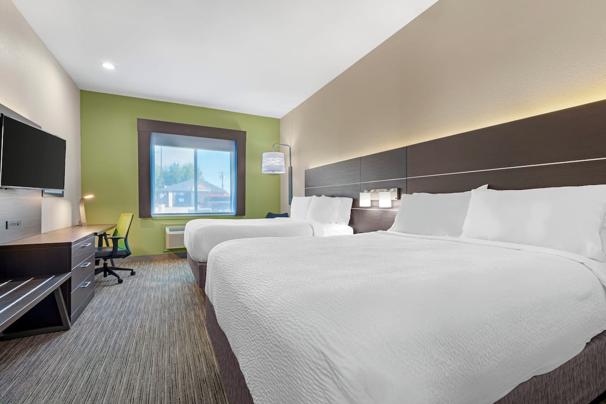 A hotel room with two beds, a desk, a chair, a TV, and a window with a view of buildings.