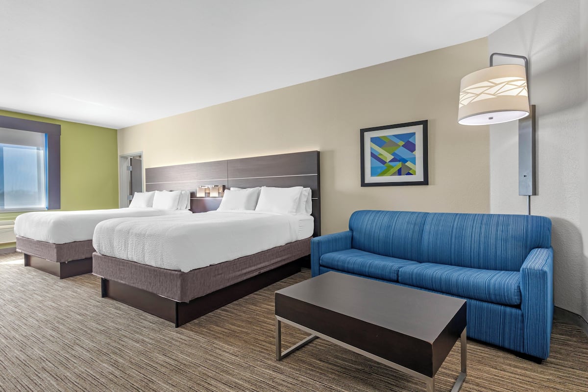 A hotel room with two beds, a blue sofa, a coffee table, a lamp, and a framed picture on the wall.