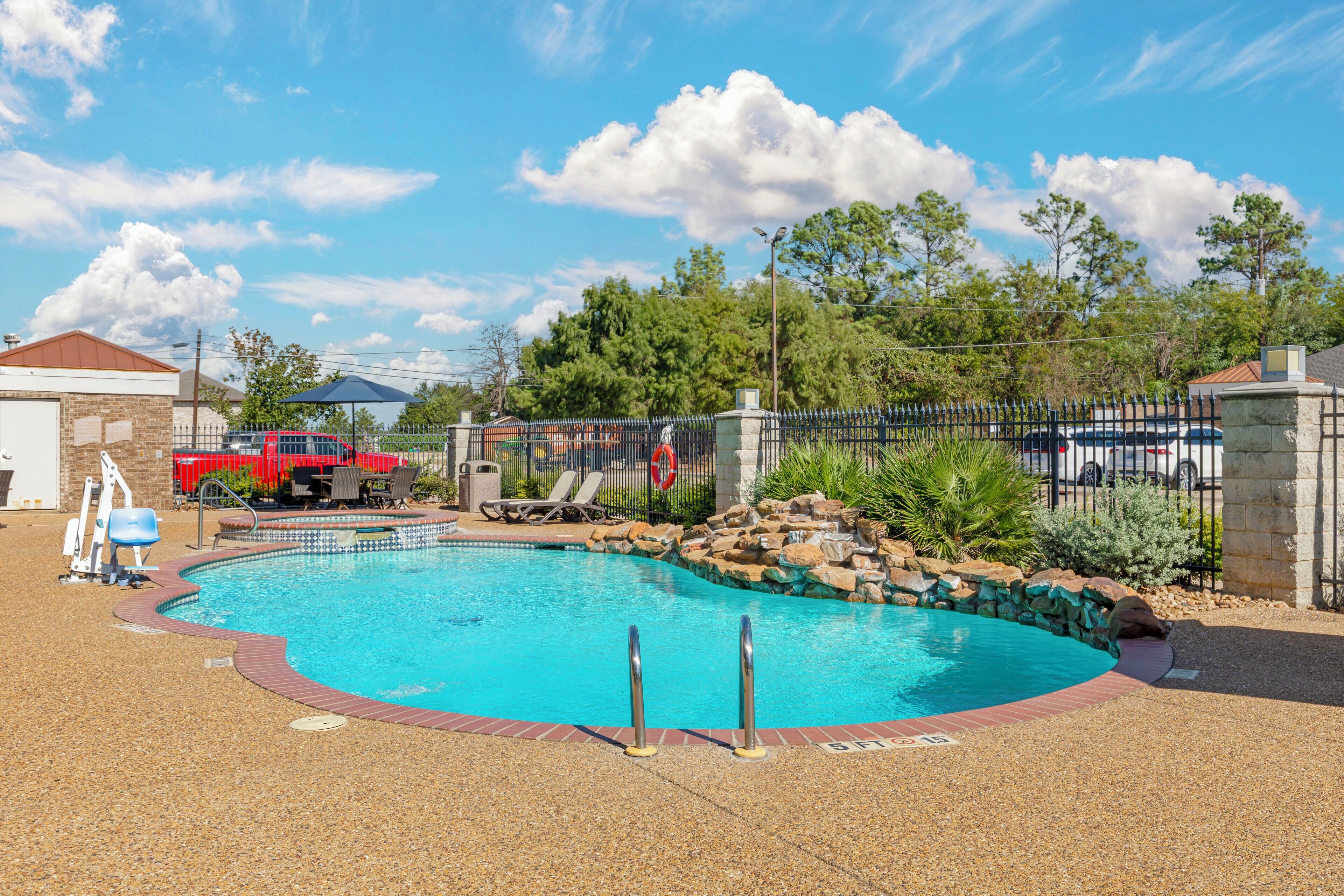 A swimming pool with a red fence, lounge chairs, and a red truck in the background.