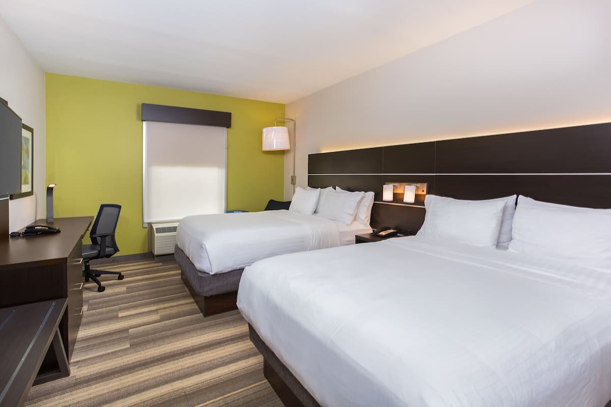 A hotel room with two beds, a desk, a chair, and a TV.
