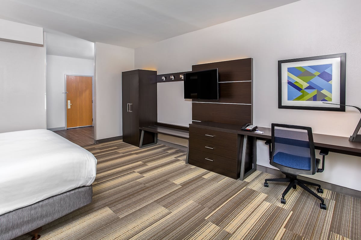 A hotel room with a bed, a desk with a chair, a TV, and a wardrobe.