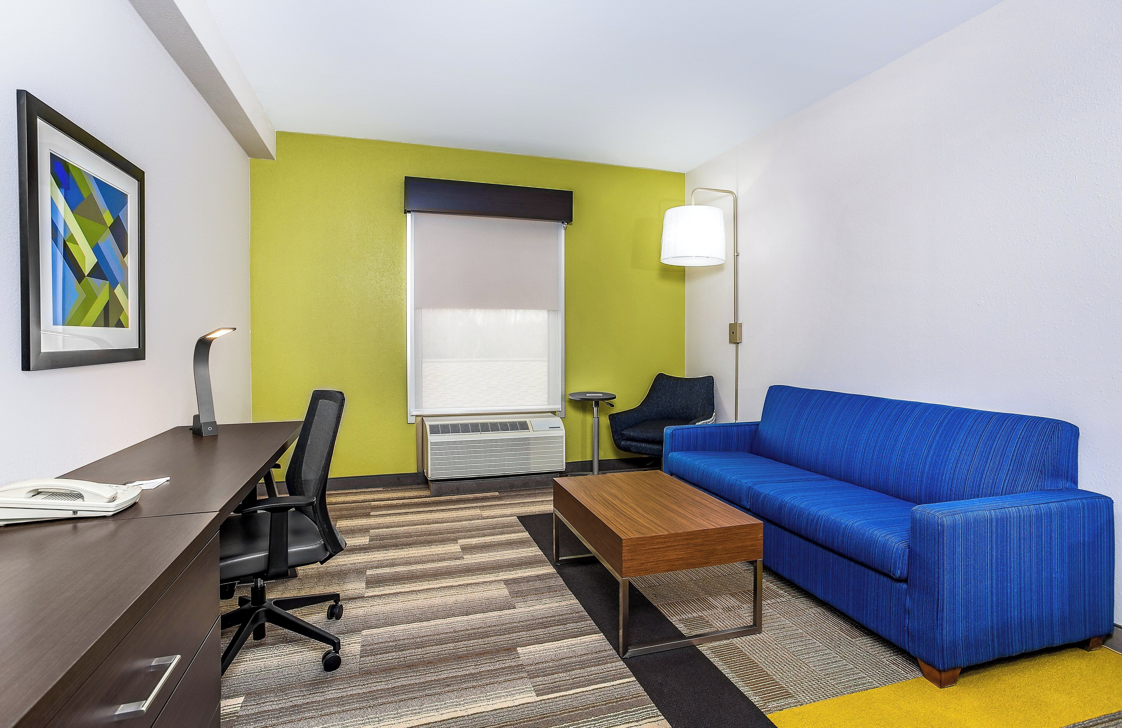 Une chambre d’hôtel avec un bureau, une chaise, un canapé bleu et une petite table.