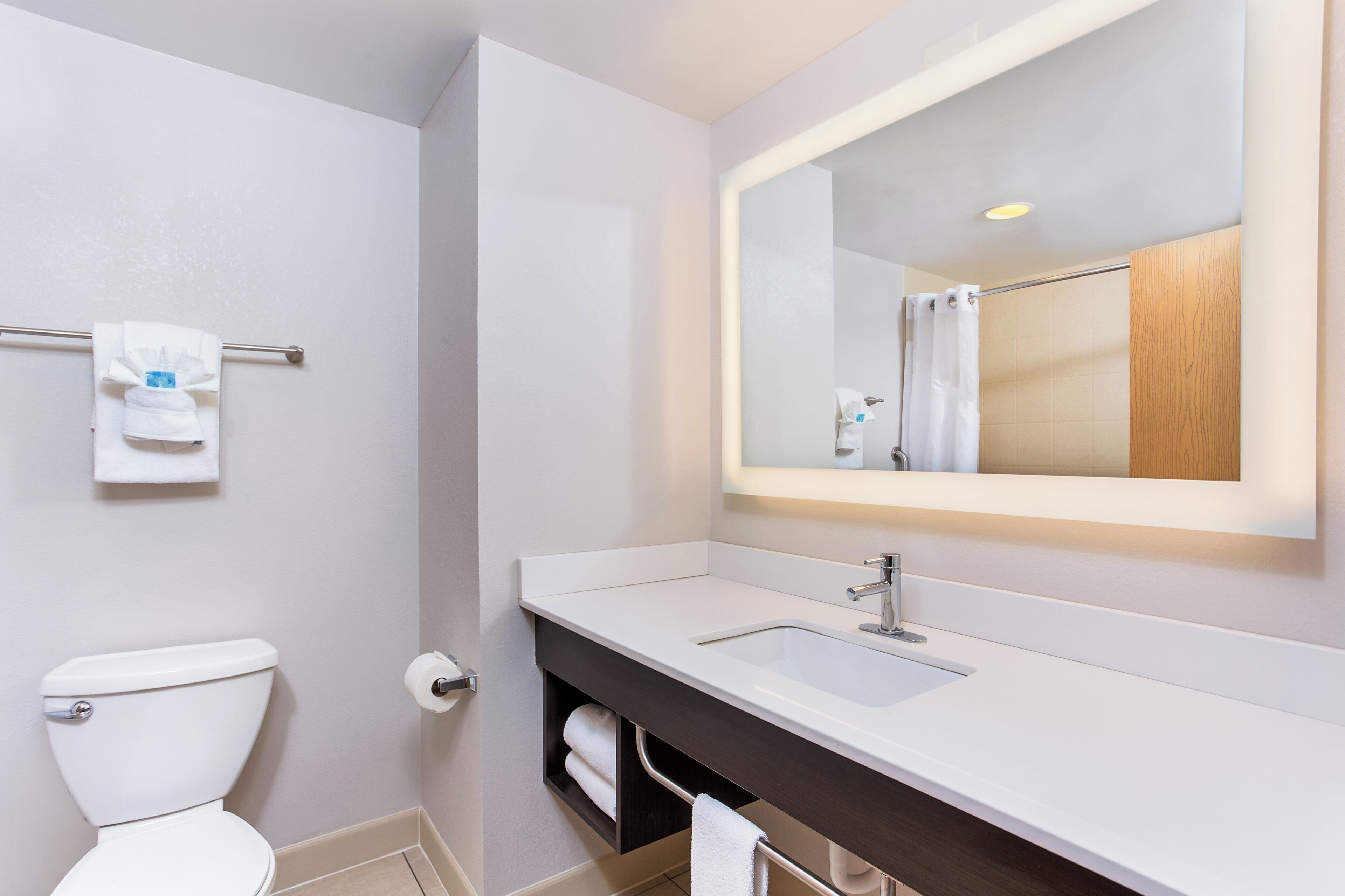 A modern bathroom with a white toilet, a sink with a dark countertop, and a mirror above the sink.