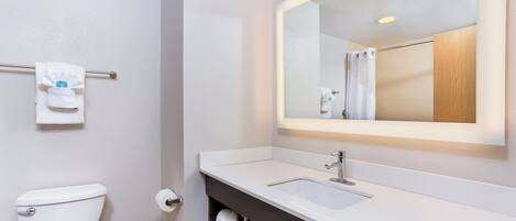 Un baño moderno con inodoro blanco, lavamanos con encimera oscura y espejo sobre el lavamanos.