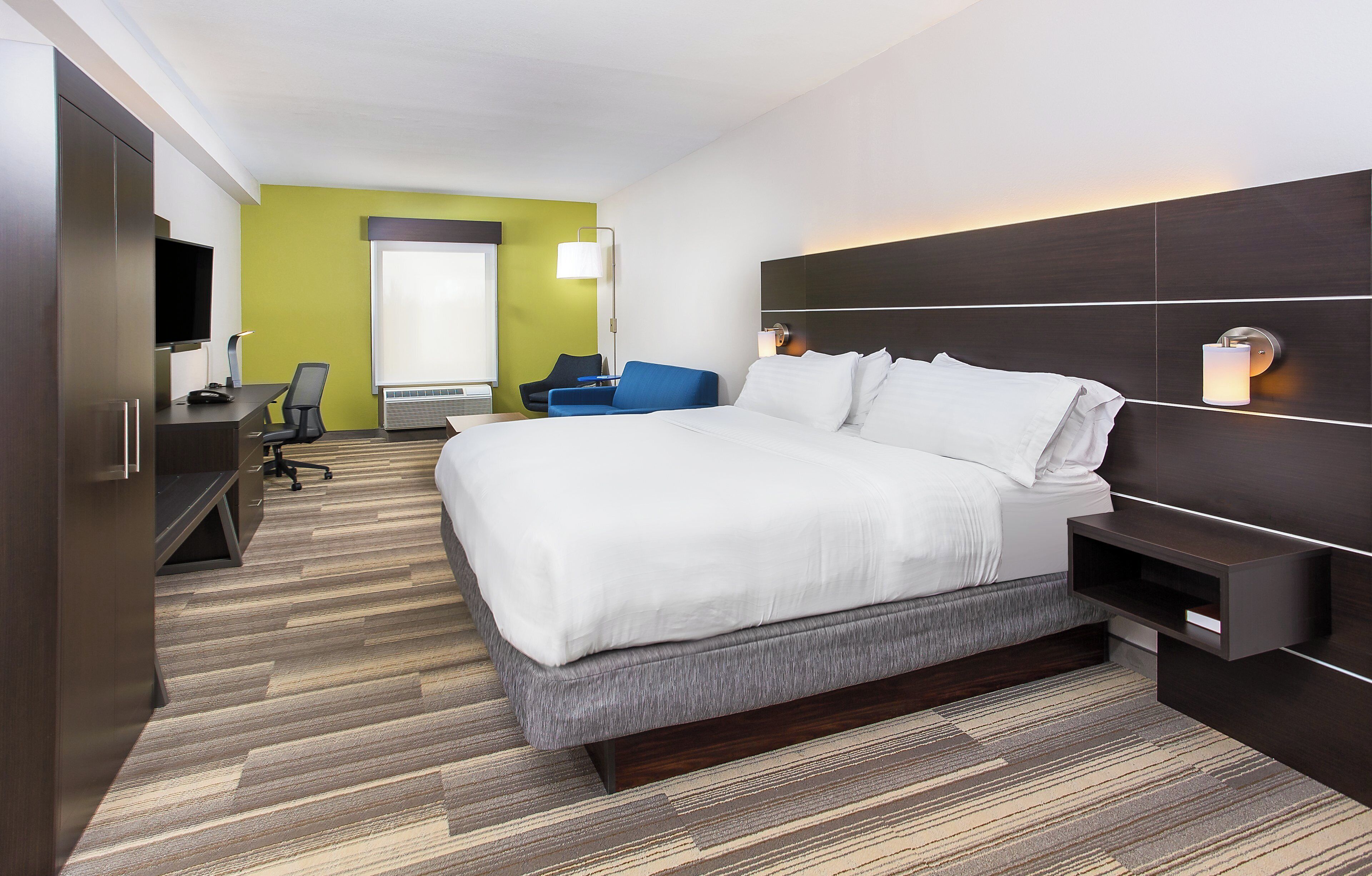 Une chambre d’hôtel équipée d’un lit, d’un bureau, d’une chaise, d’une télévision et d’un grand miroir.