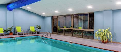 An indoor swimming pool with clear blue water, surrounded by bright yellow chairs and potted plants.