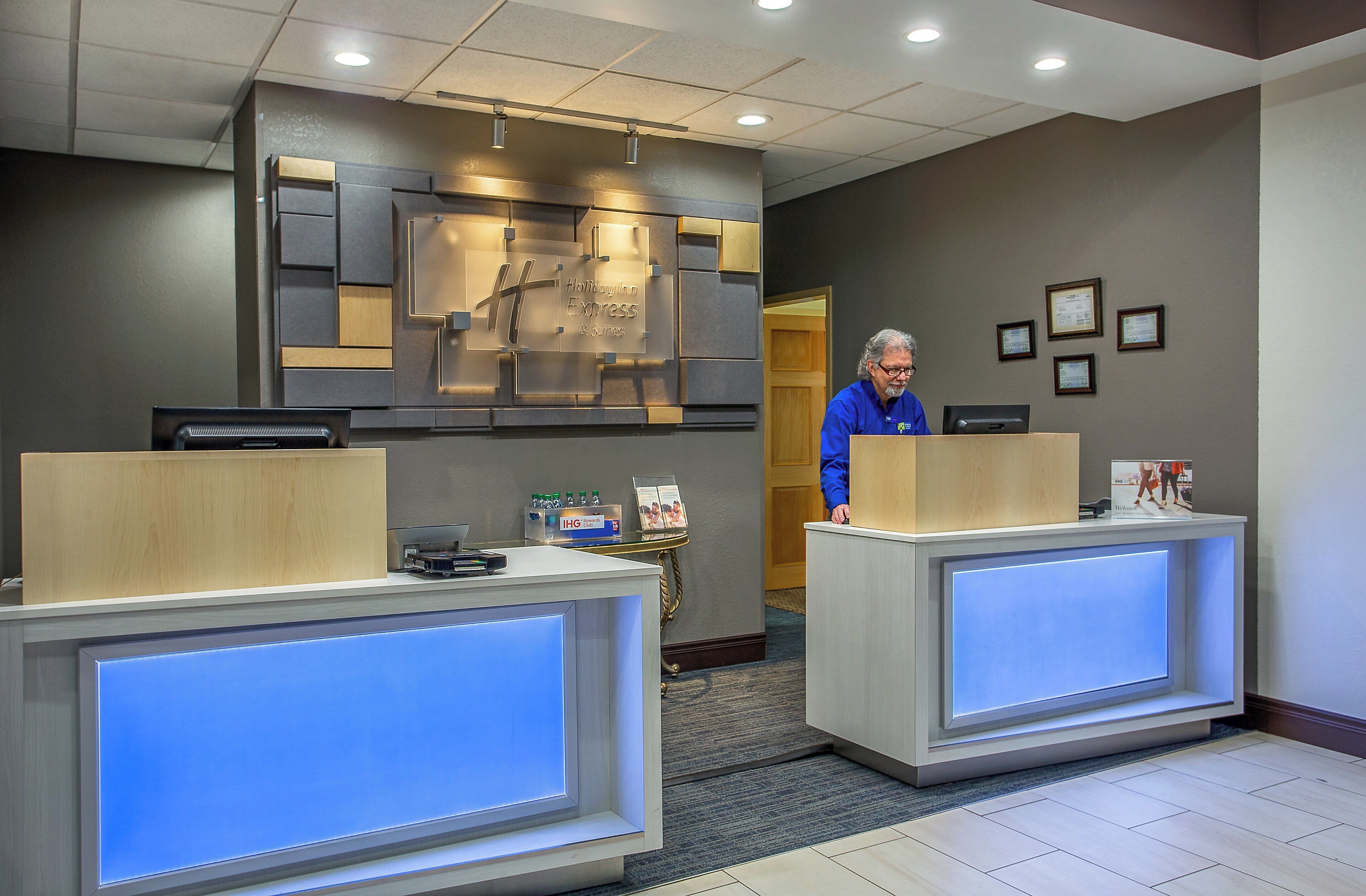 A hotel reception area with two reception desks, a wall-mounted sign, and framed certificates on the wall.