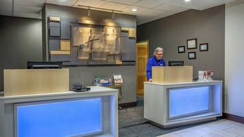 A hotel reception area with two reception desks, a wall-mounted sign, and framed certificates on the wall.