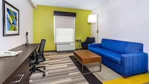 A modern hotel room with a desk, office chair, blue sofa, and a small table. - Holiday Inn Express & Suites Morristown by IHG (Morristown)