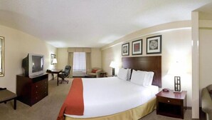 Habitación de hotel con una cama grande, un televisor sobre un mueble de madera, un escritorio con una silla y una ventana con cortinas.