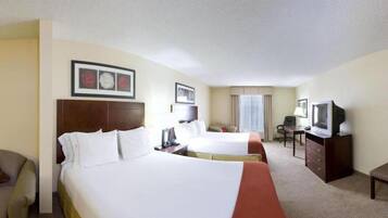 A hotel room with two beds, a desk with a television, a chair, and a window with curtains.
