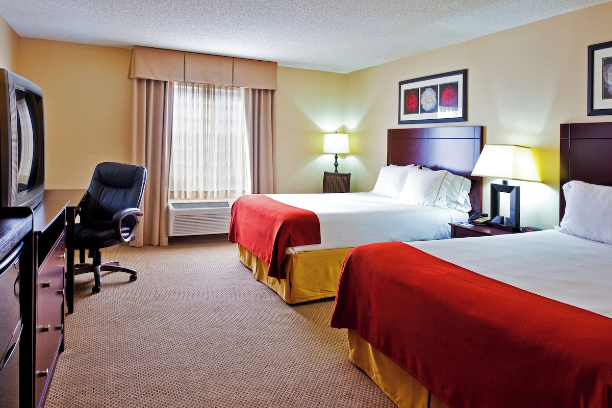 A hotel room with two beds, a desk, a chair, a television, and a window with curtains.