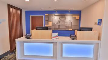 A reception desk with two computer monitors, a wooden panel, and a blue wall.