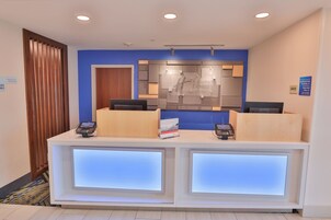 A reception desk with two computer monitors, a wooden panel, and a blue wall.
