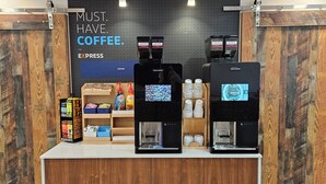 Una estación de café con dos máquinas de espresso, una exhibición de café y un cartel que dice 'MUST. HAVE. COFFEE'.