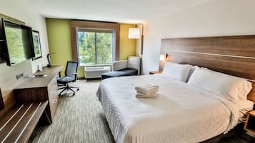 A hotel room with a bed, desk, chair, and a large window.