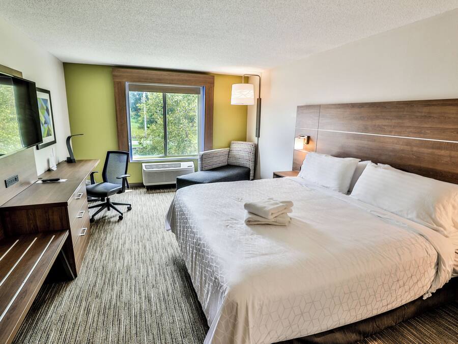 A hotel room with a bed, desk, chair, and a large window.