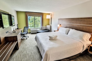 A hotel room with a bed, desk, chair, and a large window.