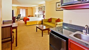 Habitación de hotel con cama, sofá, mesa de comedor, zona de cocina con microondas y televisor.