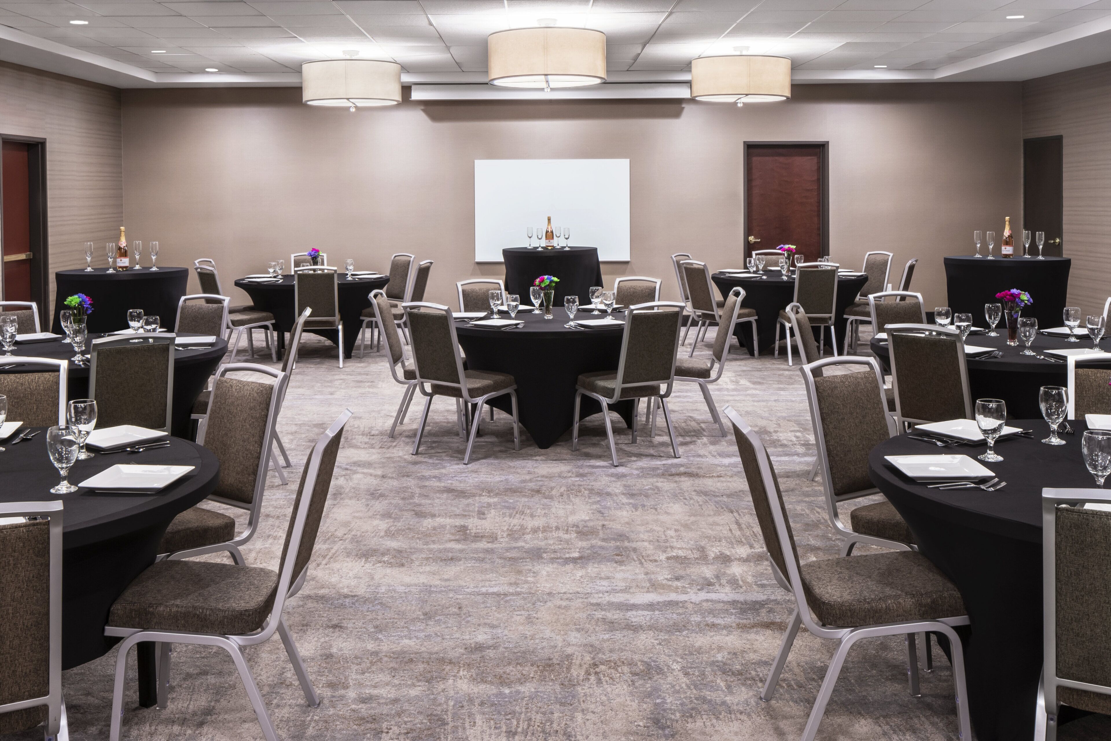 A conference room with multiple tables, chairs, and a projector screen.