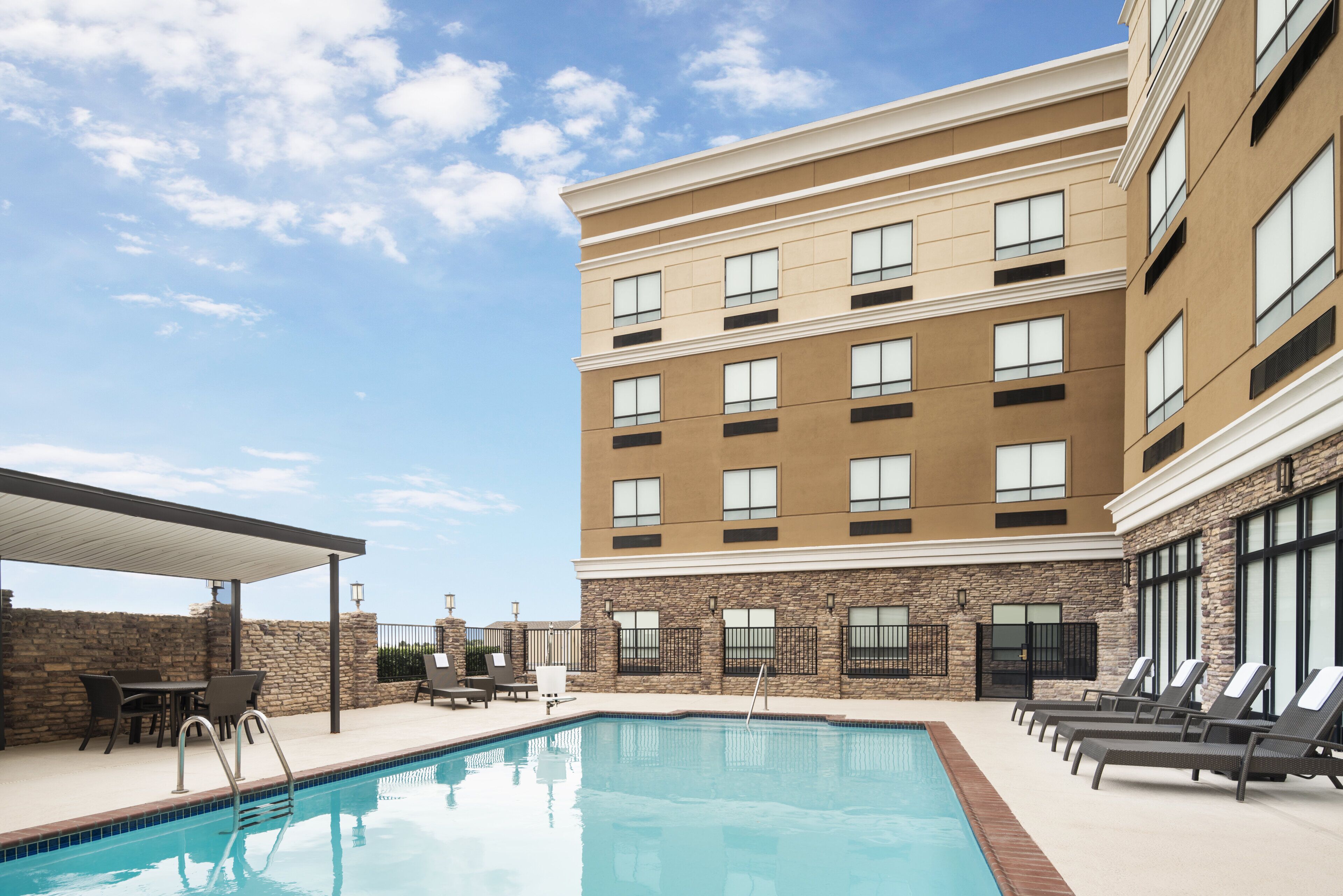 A hotel with a swimming pool, outdoor seating, and a covered patio area.