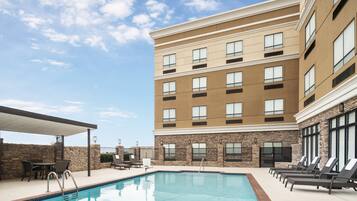 A hotel with a swimming pool, outdoor seating, and a covered patio area.