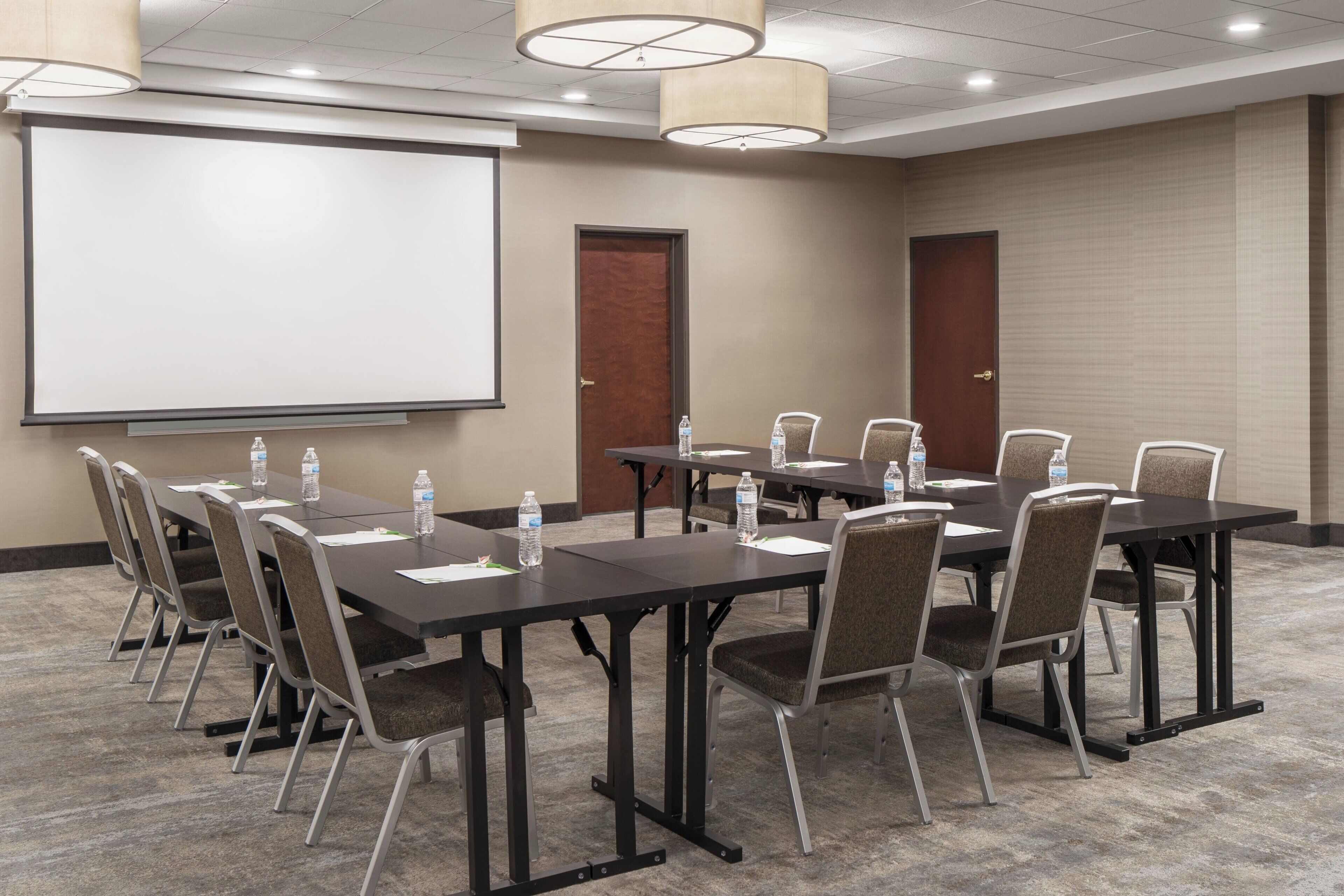 A conference room with a large screen, multiple tables, and chairs.