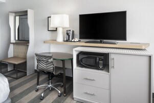 Habitación de hotel con cama, escritorio con computadora, silla, televisor, cafetera y microondas.