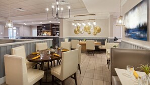 Ein modernes Restaurant mit einem zentralen Essbereich, einer Bar und einer Sitzecke mit Blick auf die Stadtlandschaft.