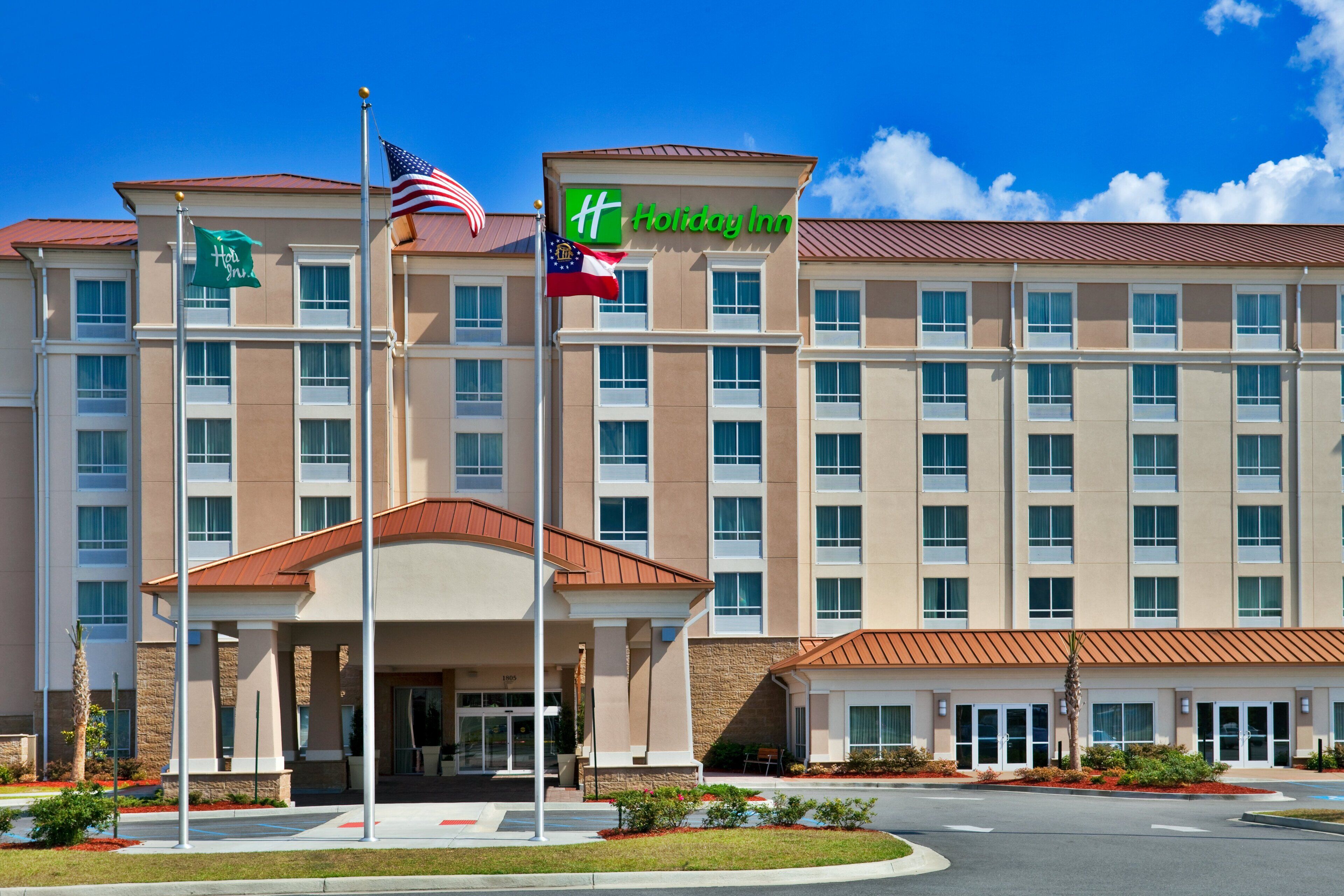 A Holiday Inn hotel with a central entrance, multiple floors, and a flagpole with the American flag.