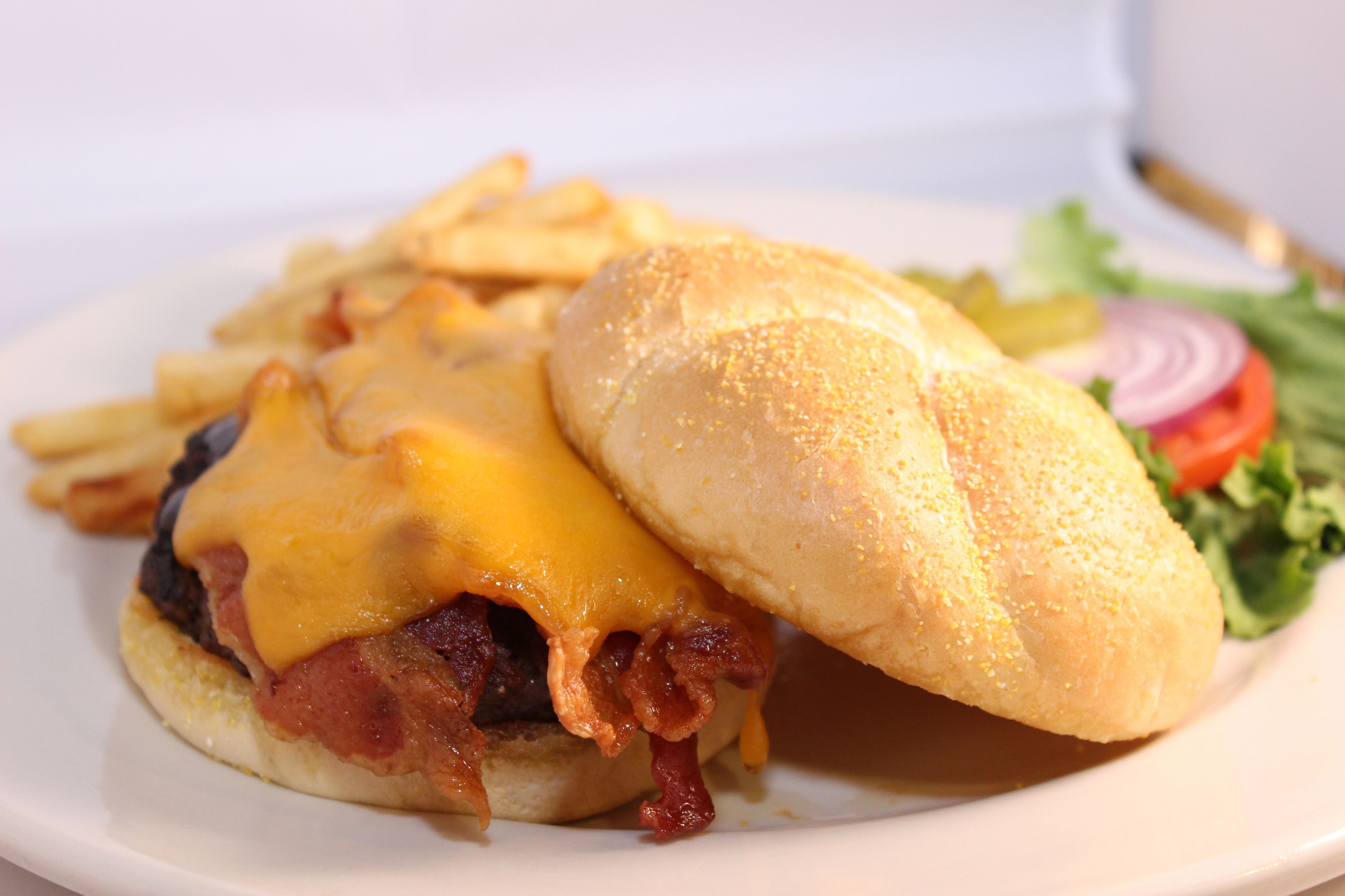 A sandwich with melted cheese, bacon, and a side of fries.