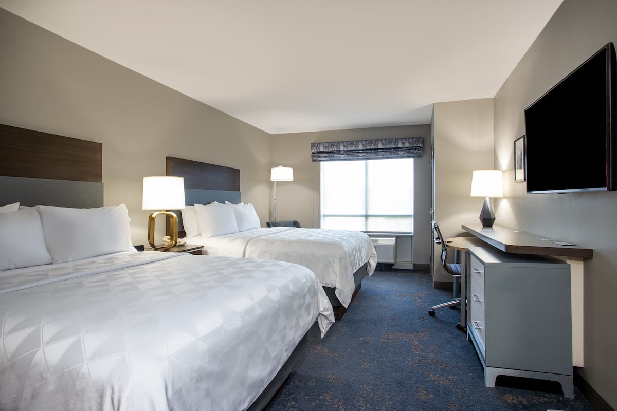 A hotel room with two beds, a desk, a chair, a TV, and a window with a view.
