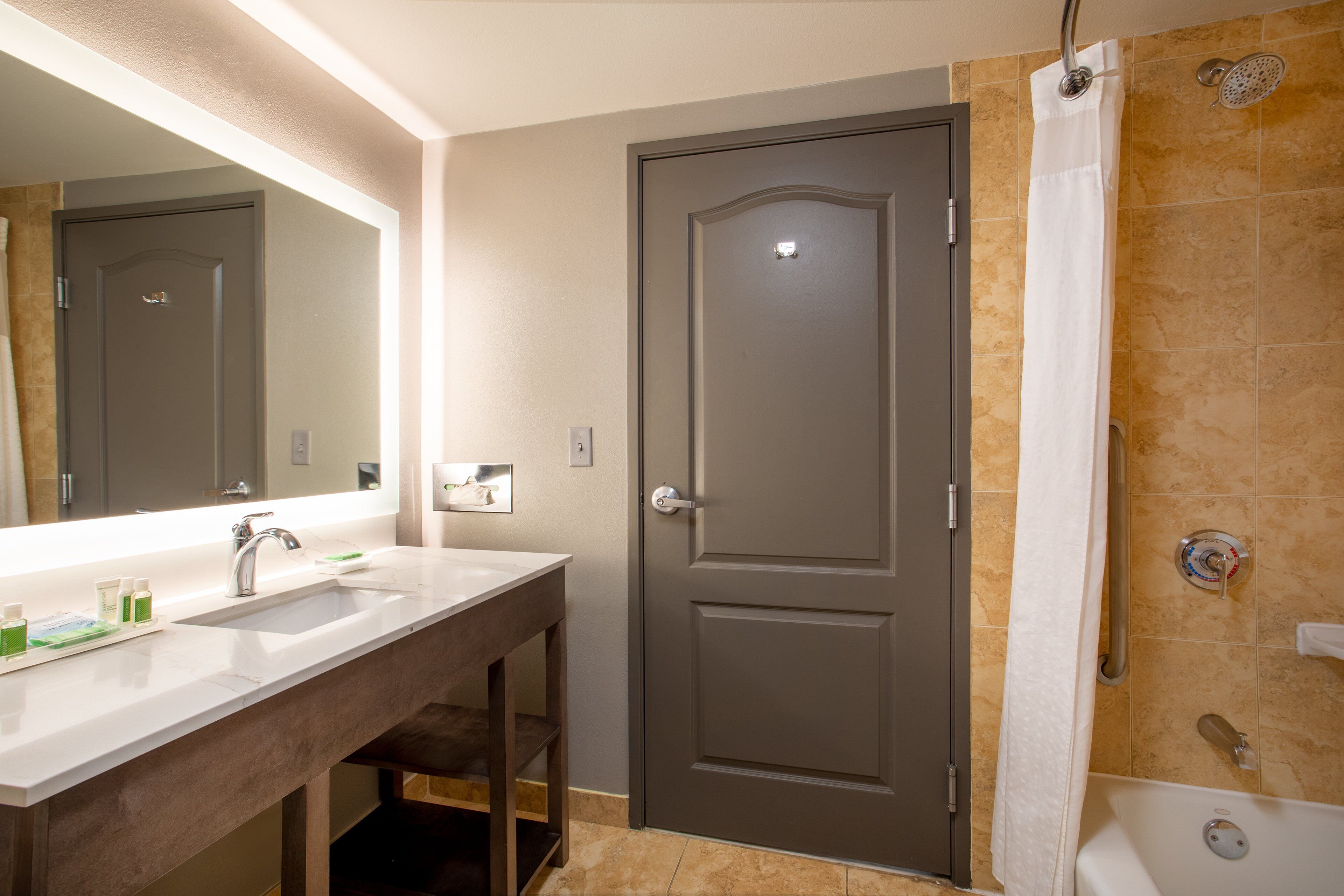 A bathroom with a double sink, a shower, and a door with a handle.