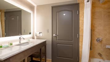 A bathroom with a double sink, a shower, and a door with a handle.