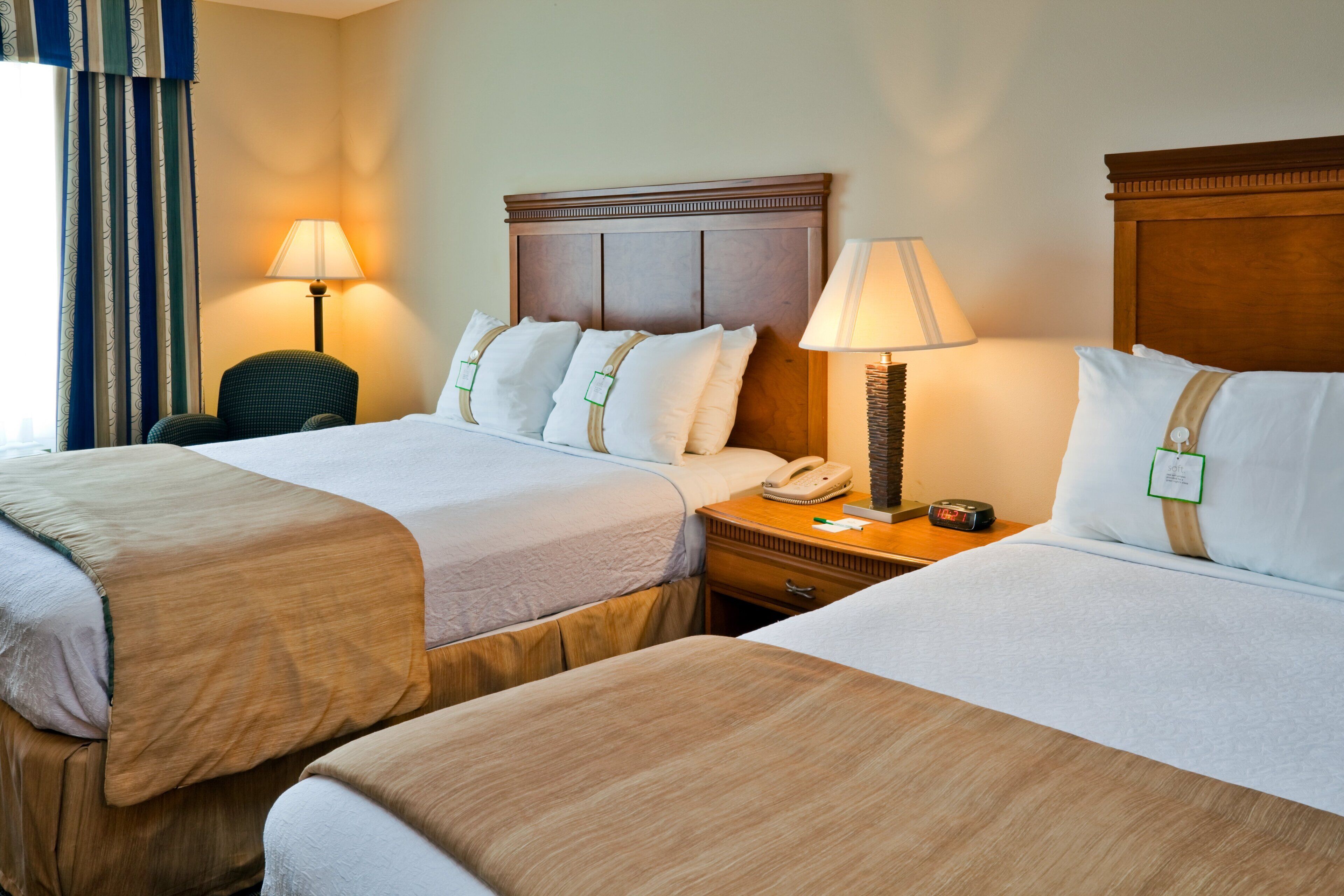 Une chambre d’hôtel avec deux lits, une table de chevet avec une lampe, un téléphone et une chaise.