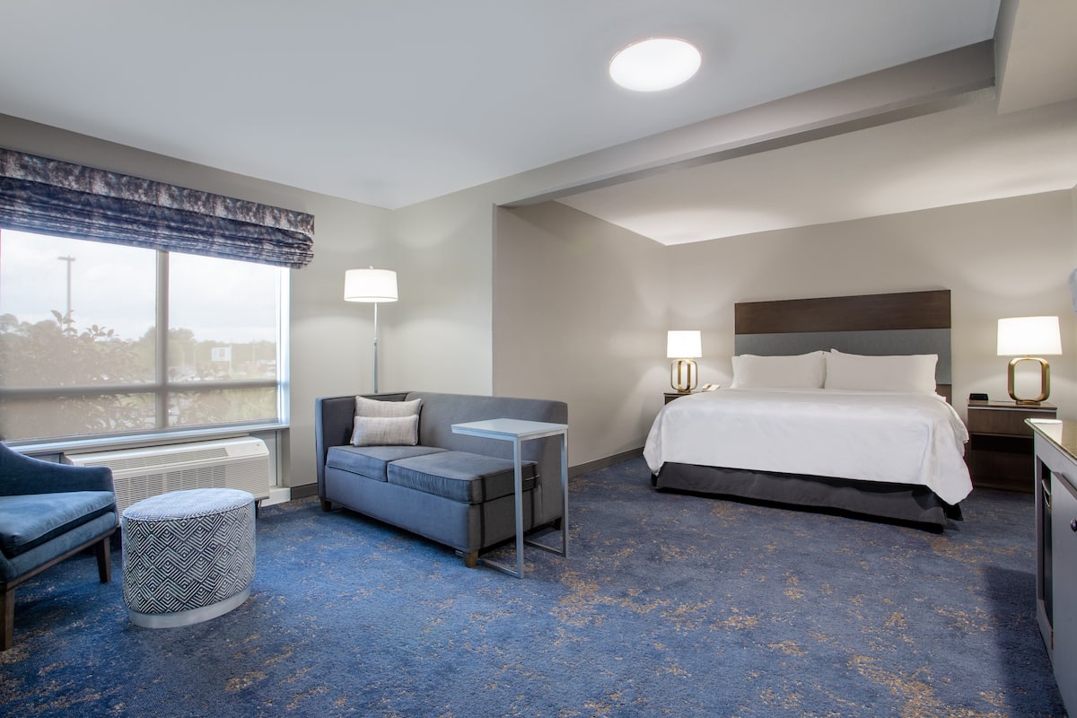 A hotel room with a bed, a sofa, a small table, and a window with a view.