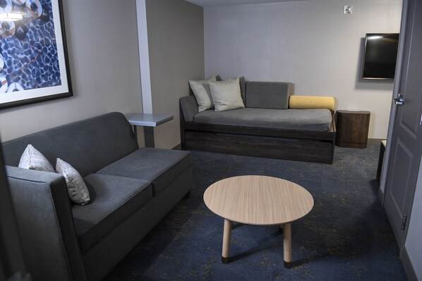 A modern living room with a grey sofa, a smaller grey couch, a round wooden coffee table, and a grey carpet.