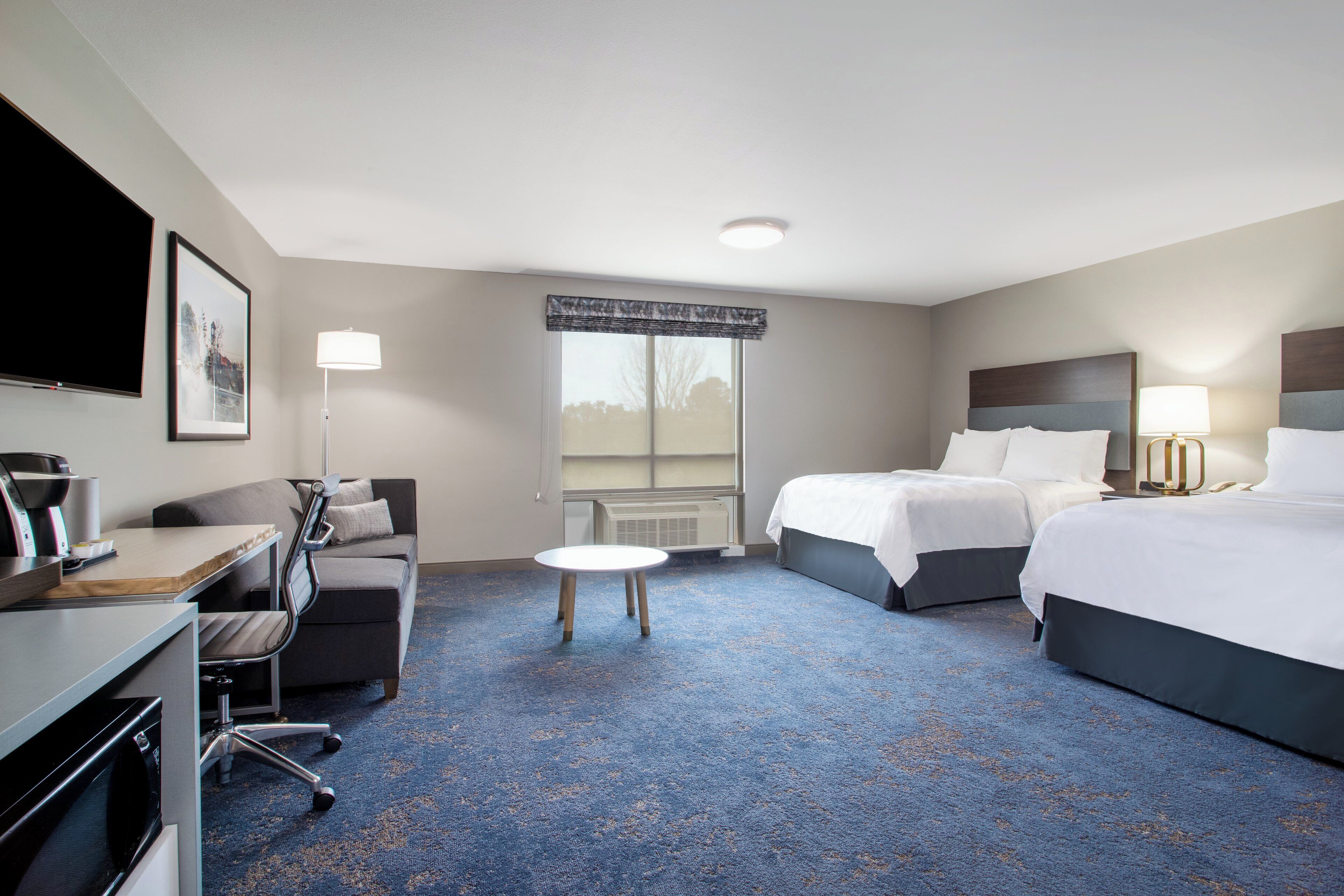 A hotel room with a bed, a desk, a chair, a small table, and a television.