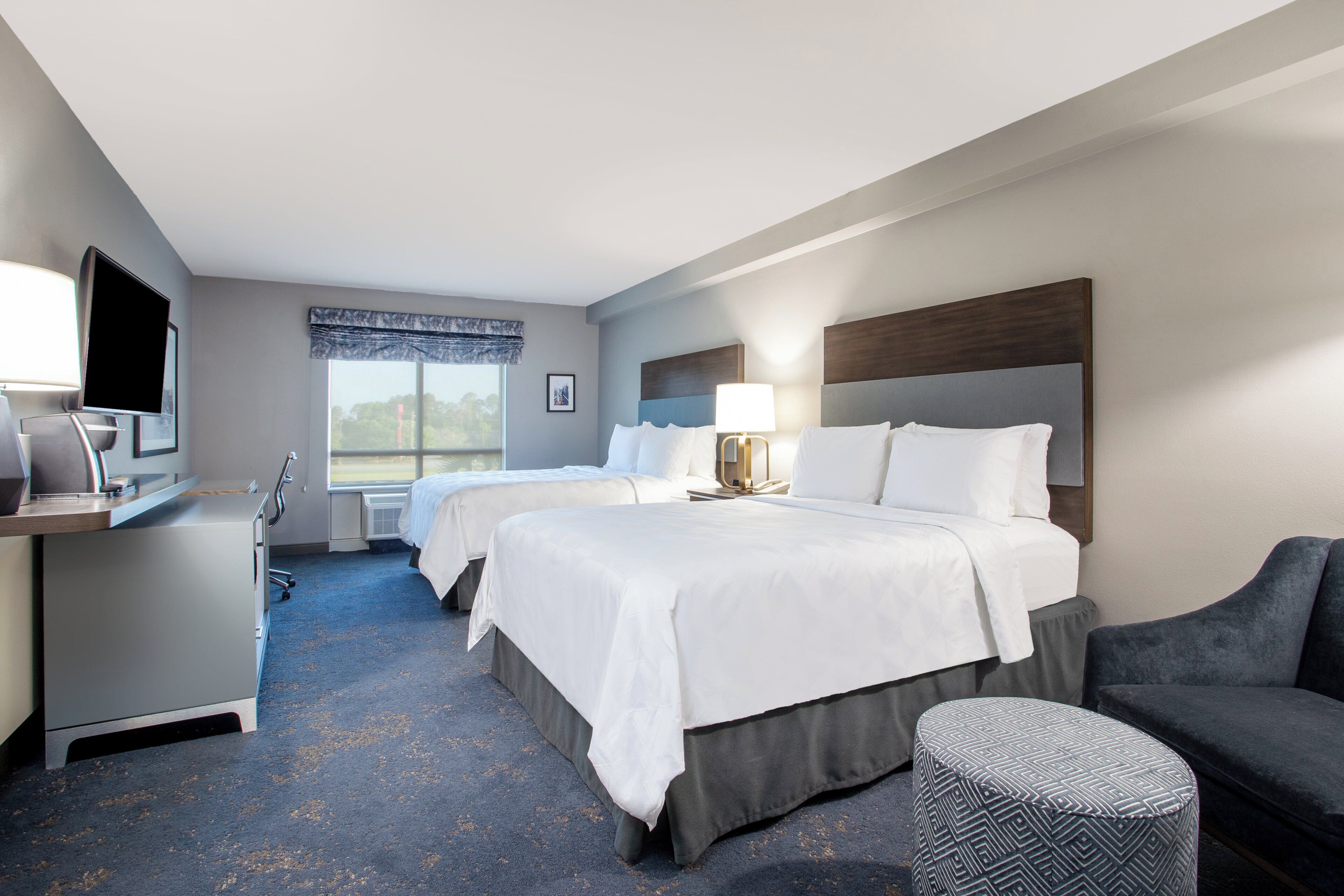 A hotel room with two beds, a desk with a flat-screen TV, a chair, and a couch.
