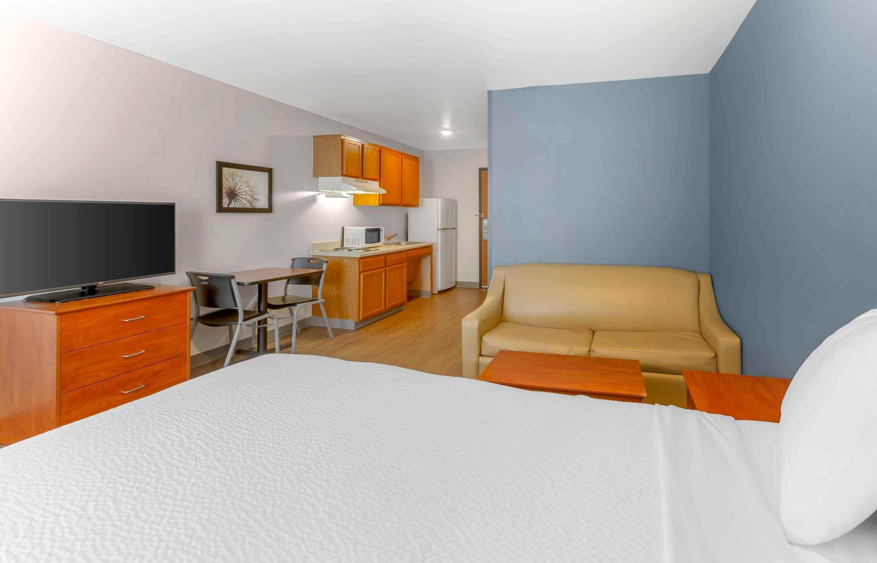 A hotel room with a bed, a desk with a chair, a kitchenette, and a sofa.