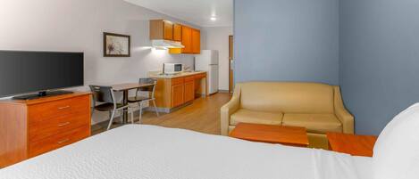 Una habitación de hotel con cama, escritorio, silla, kitchenette y sofá.