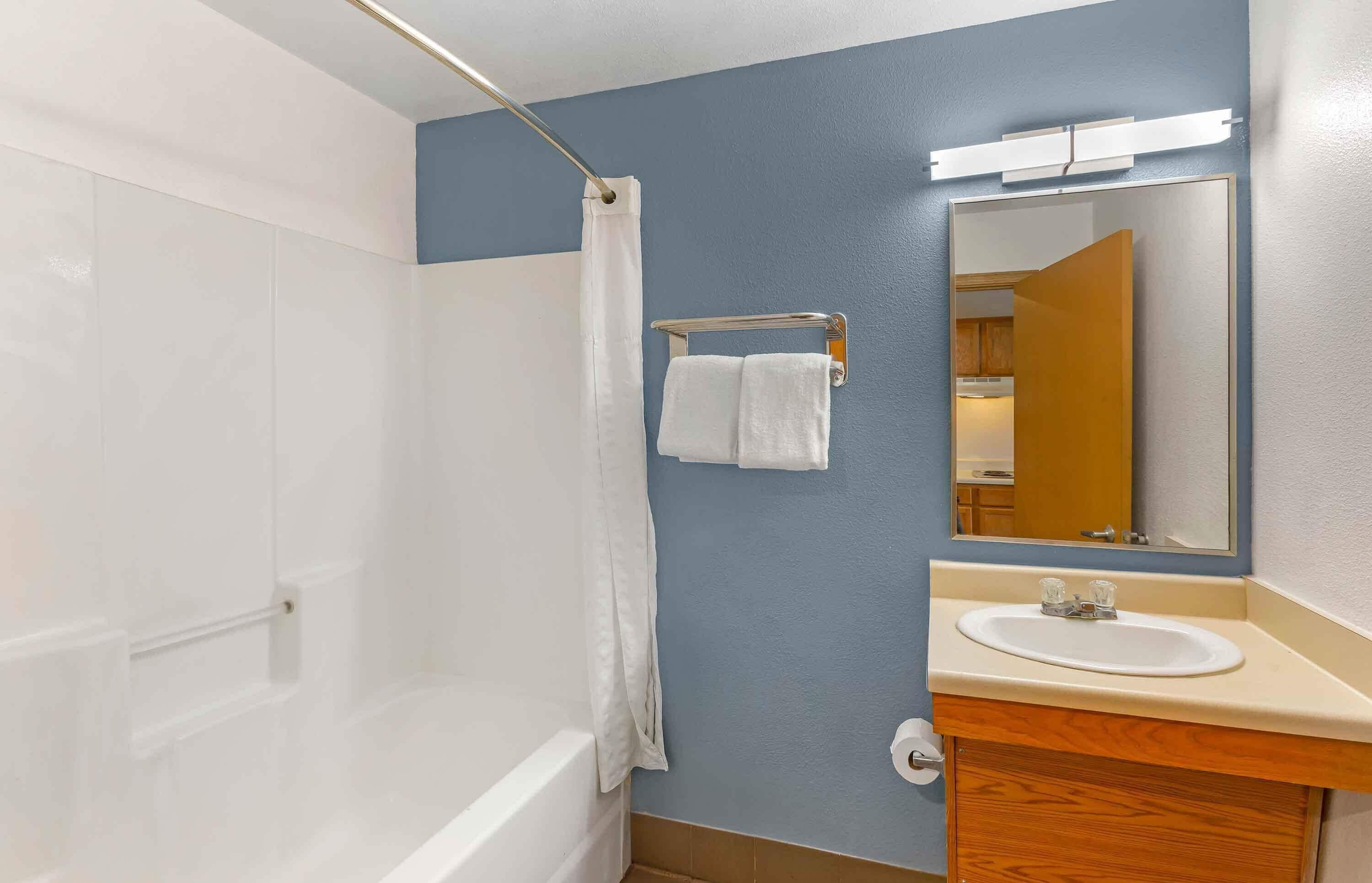 A bathroom with a bathtub, a sink, a mirror, and a towel rack.