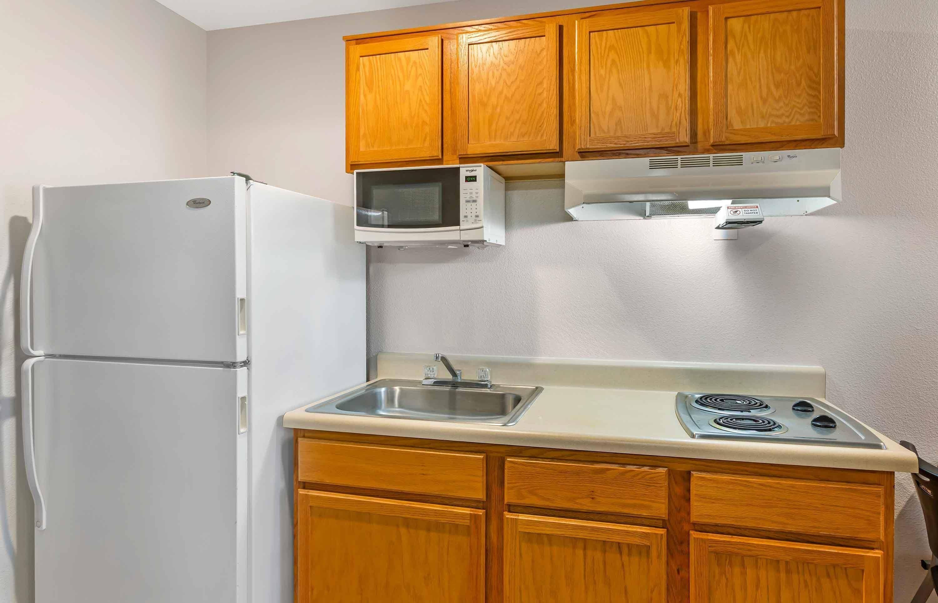 Una cocina compacta con armarios de madera, un refrigerador blanco, un microondas, un fregadero y una estufa.