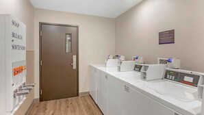 A laundry facility with a door, a wall-mounted sign, and multiple washing machines. - Extended Stay America Select Suites - Las Cruces (Las Cruces)