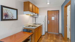 A compact kitchen with wooden cabinets, a microwave, a refrigerator, a sink, and a dining table. - Extended Stay America Select Suites - Las Cruces (Las Cruces)